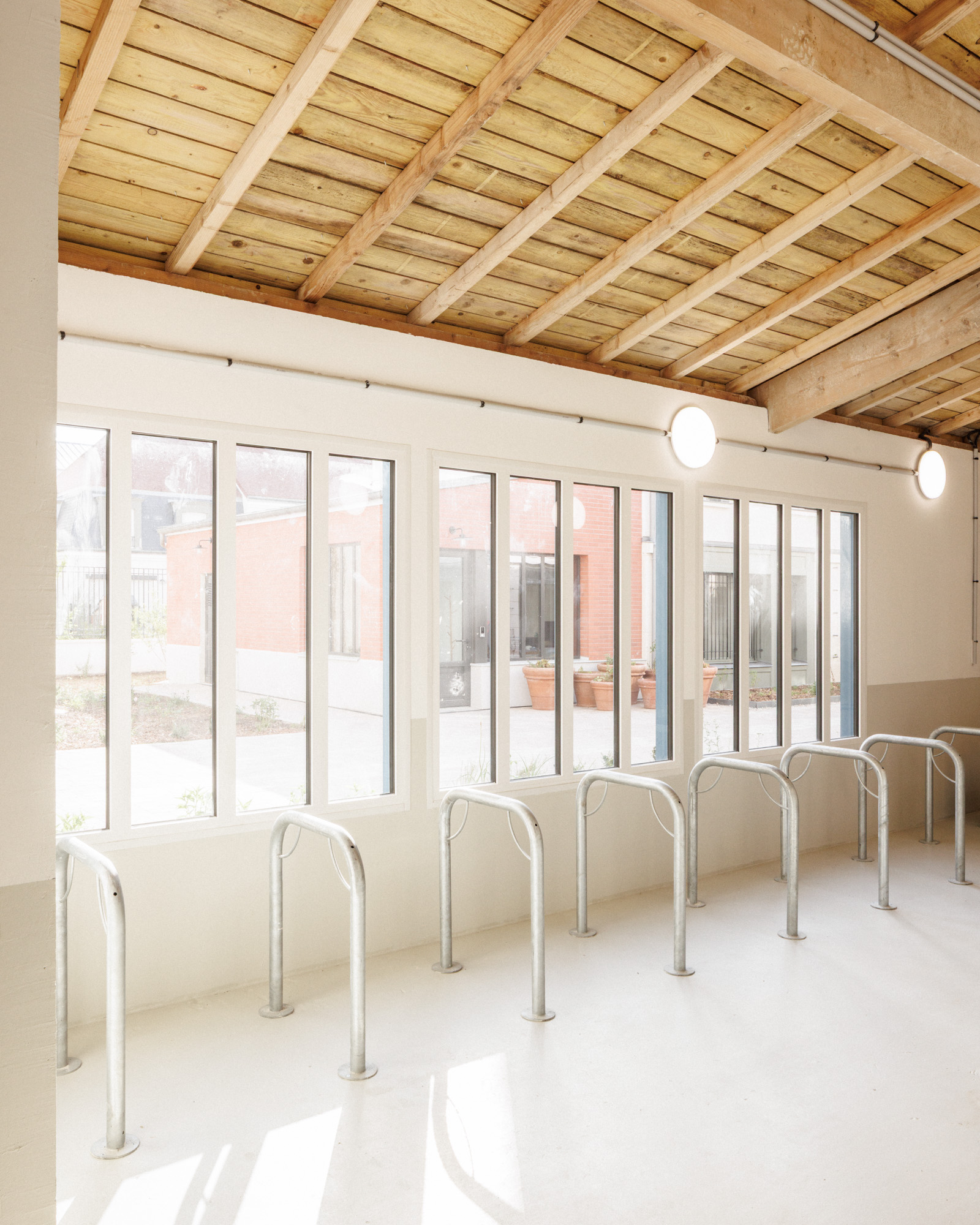 Local vélo moderne à charpente bois apparente et vue sur cour, du projet de 47 logements sociaux à Serris par Cussac Architectes et Associés (CA+A)